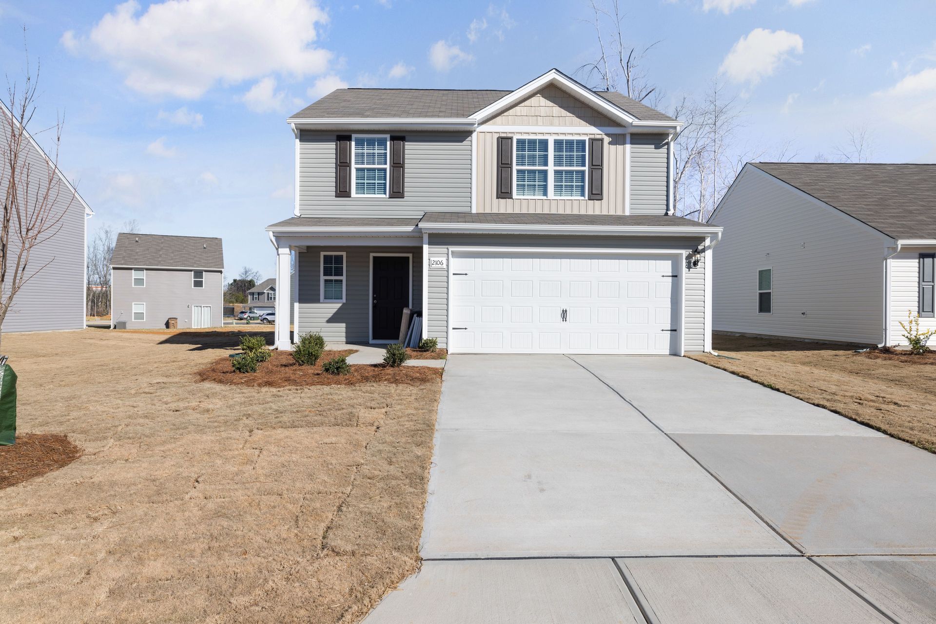Two-story suburban house with a white garage and concrete driveway under a partly cloudy sky