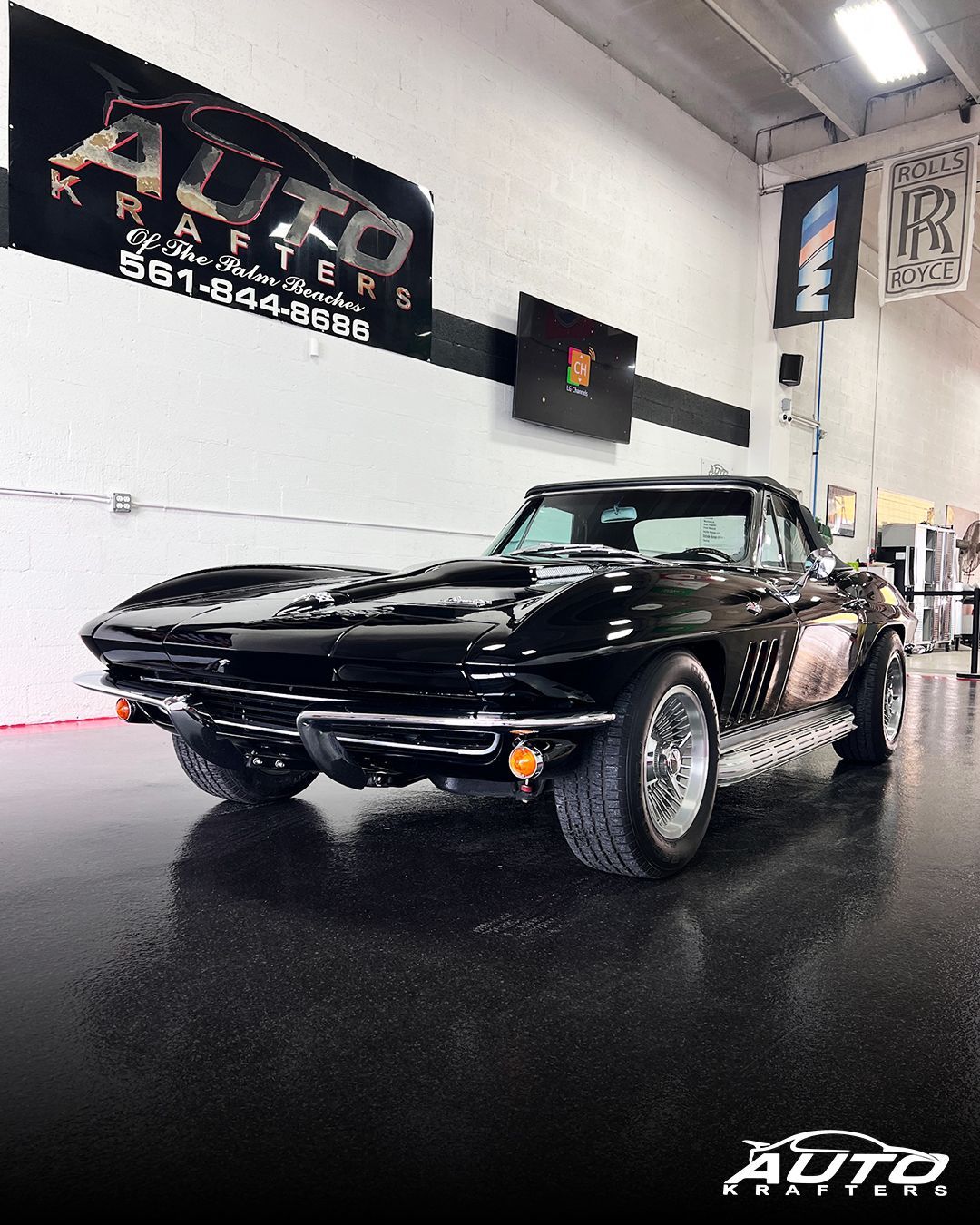 Black classic convertible car, likely a Corvette, parked inside a showroom.