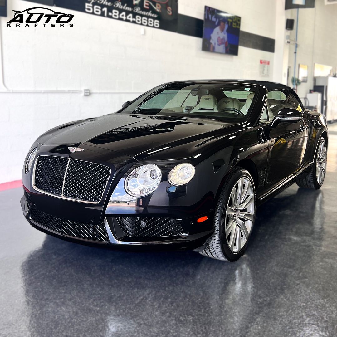 Black Bentley convertible on a polished floor in a showroom setting with the business name in the background.