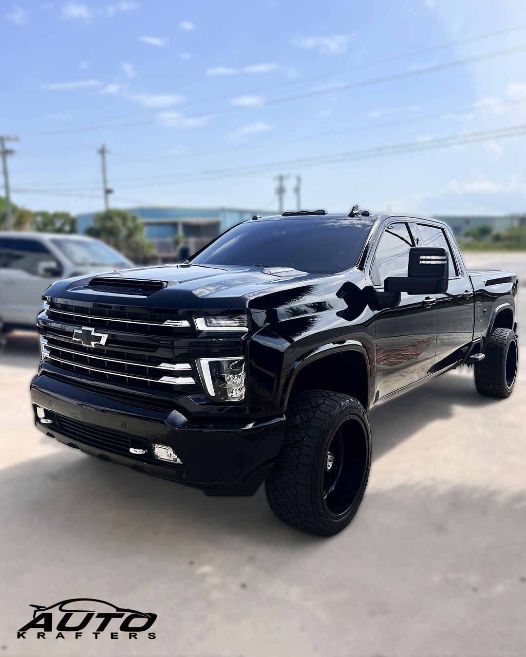 Black Chevrolet pickup truck with large black wheels, parked outdoors on a sunny day.