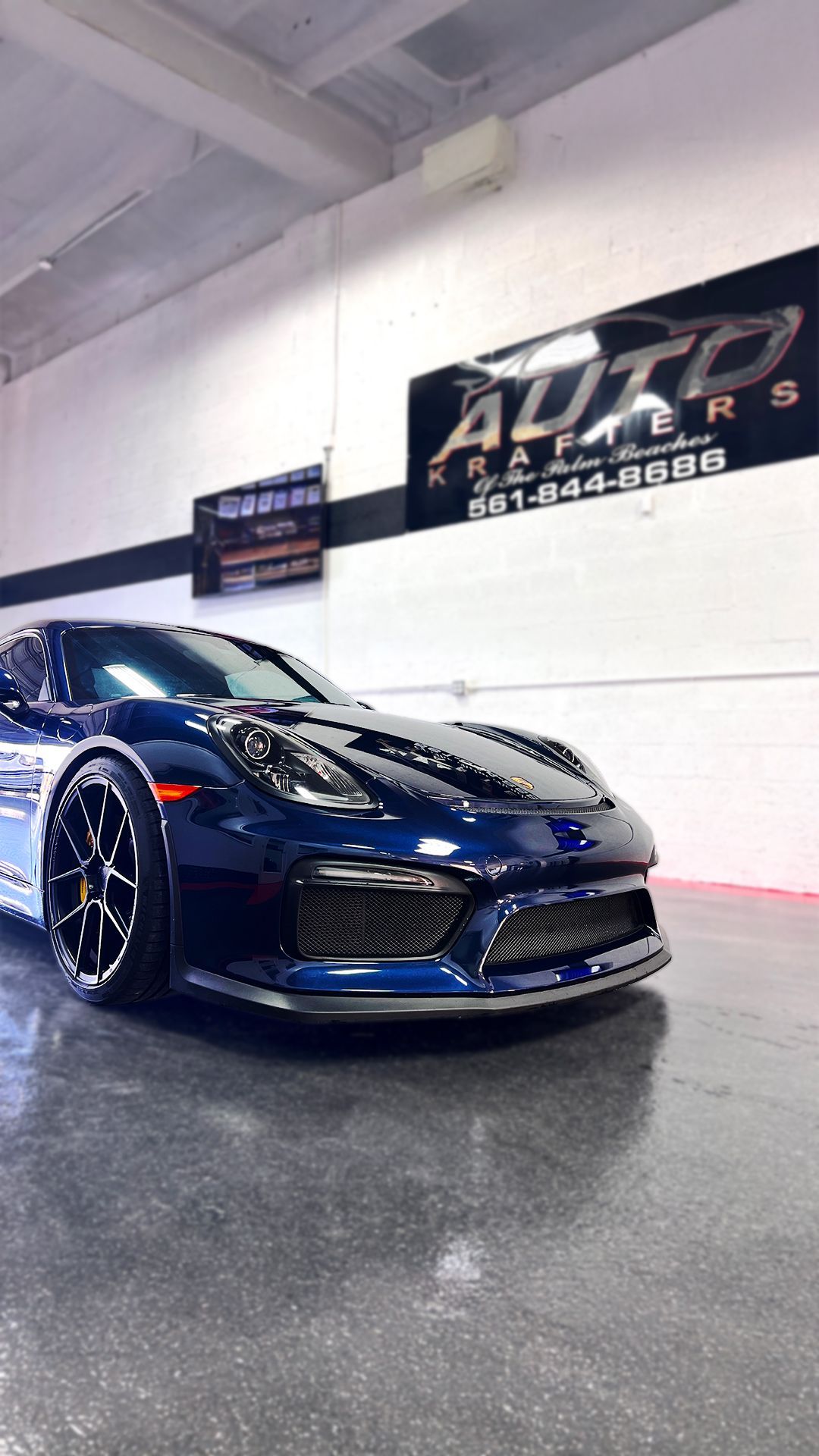 Dark blue sports car parked inside a shop, with a sign that says 