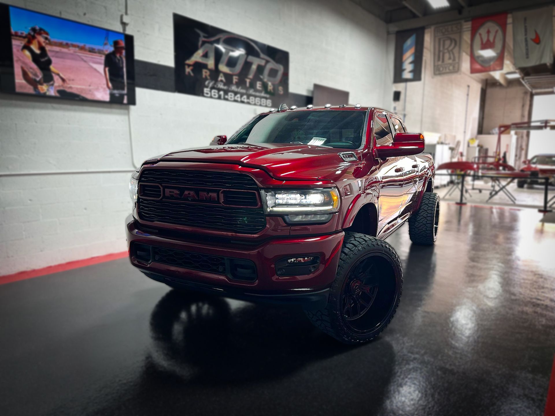 Red lifted pickup truck in a garage with black wheels. Auto detailing business sign in the background.