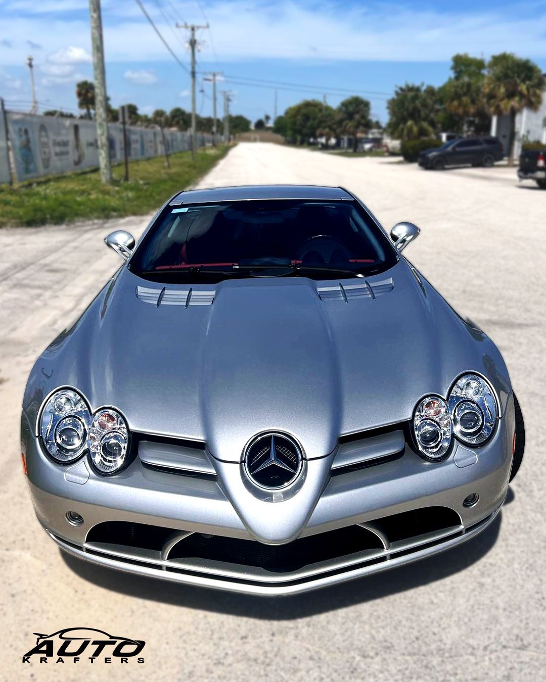 Silver Mercedes-Benz SLR McLaren sports car parked on a road, sunny day.