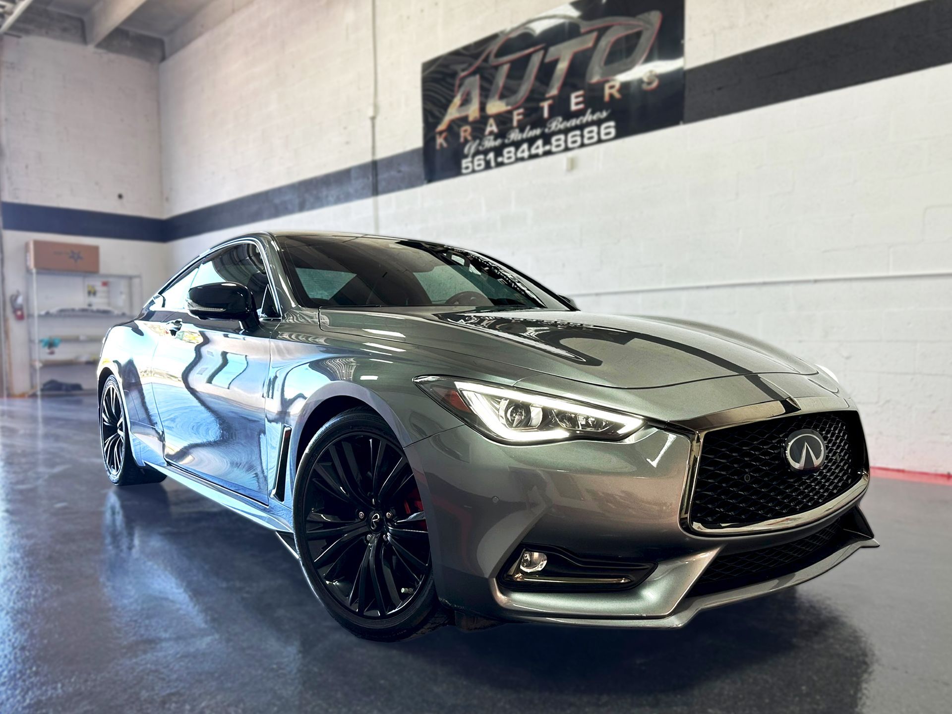 Gray Infiniti Q60 coupe with black wheels inside a shop.