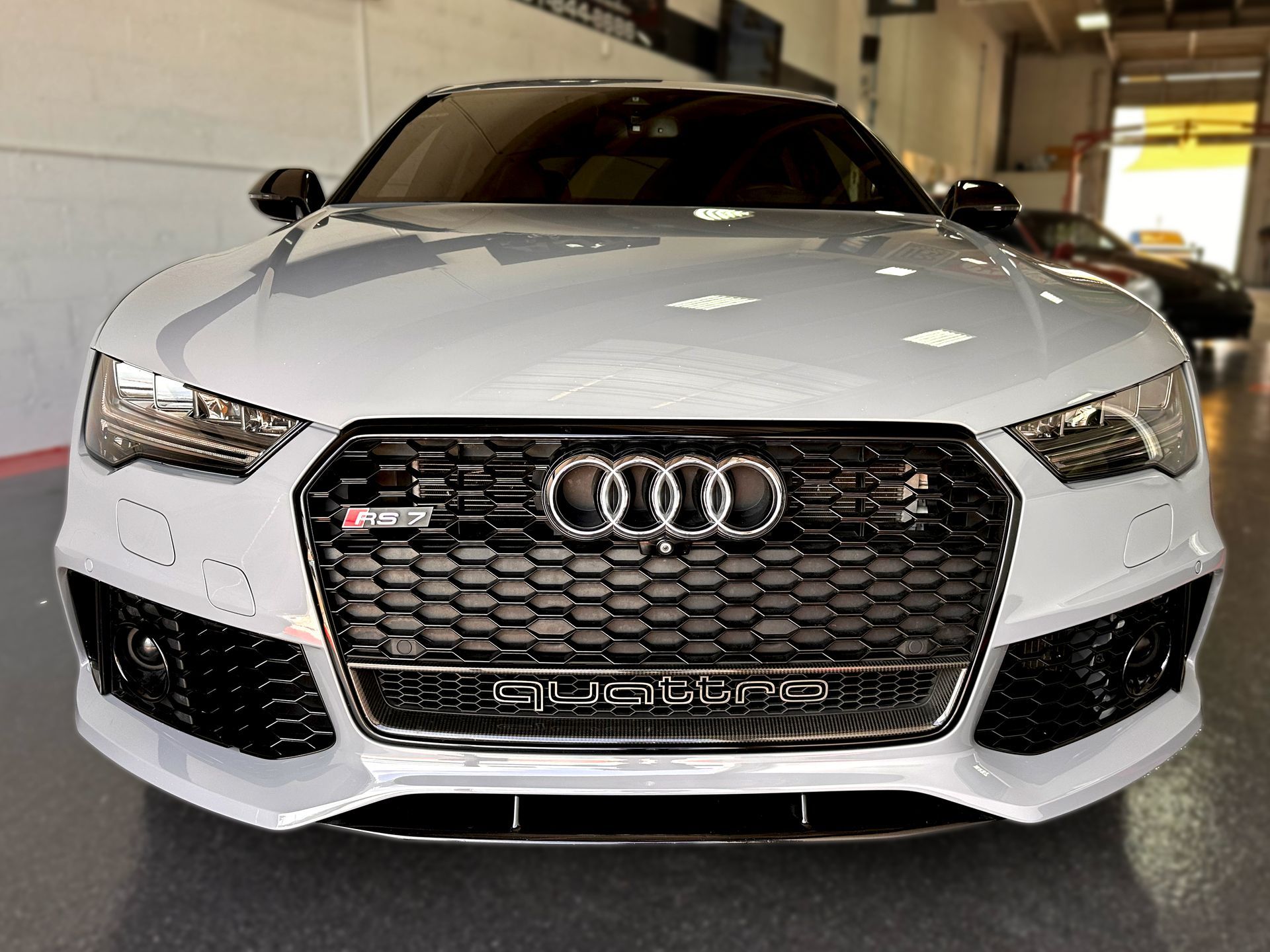 White Audi RS7 sports car with black grill and accents, parked indoors.