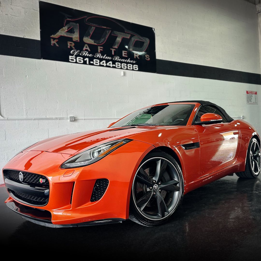 Orange Jaguar sports car in a garage with Auto Krafters sign.