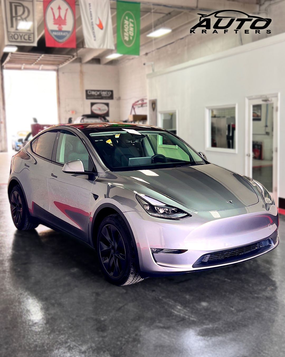 Silver Tesla Model Y car in a garage with brand flags overhead.
