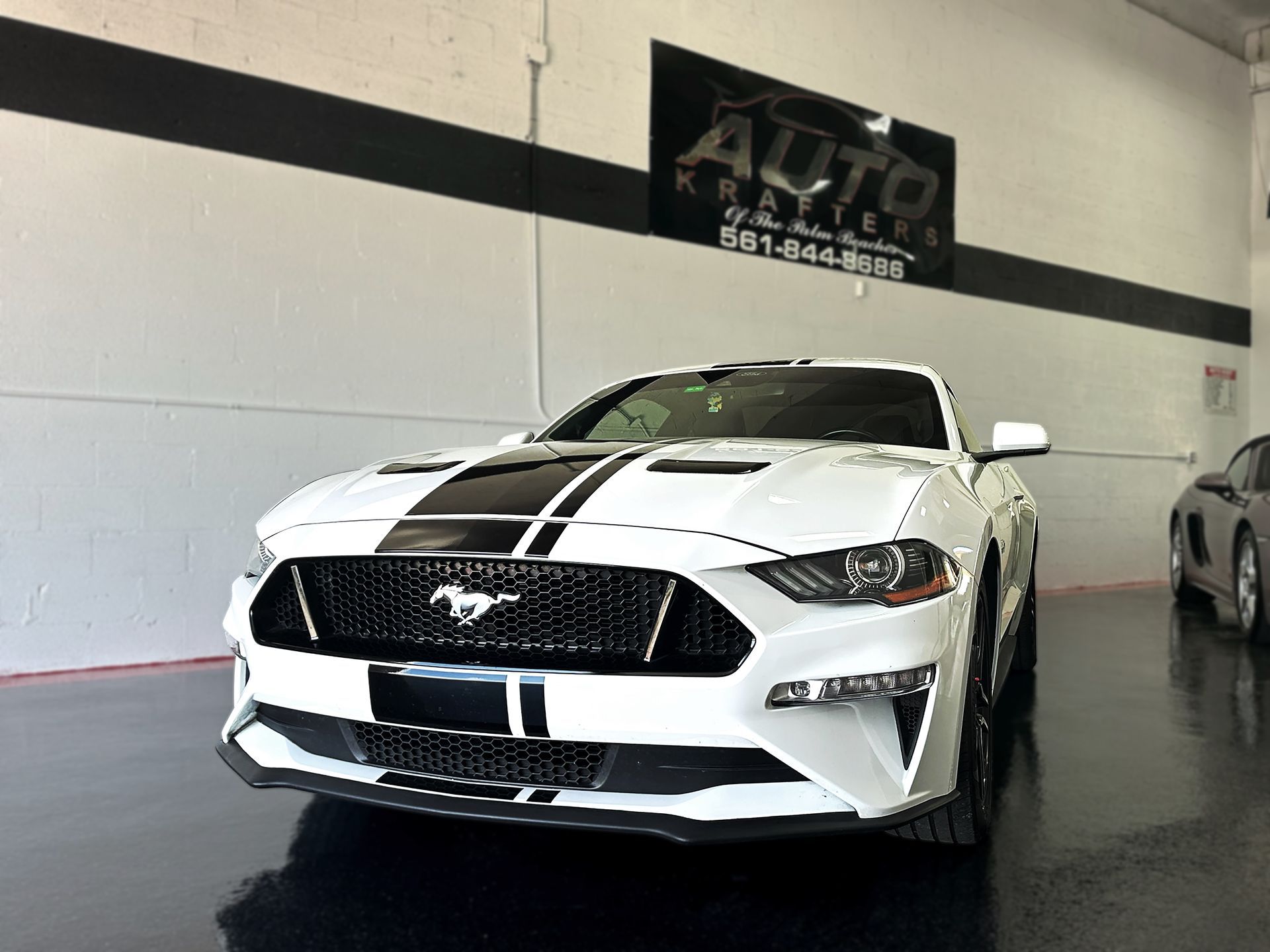 White Ford Mustang with black racing stripes, parked inside a car dealership.