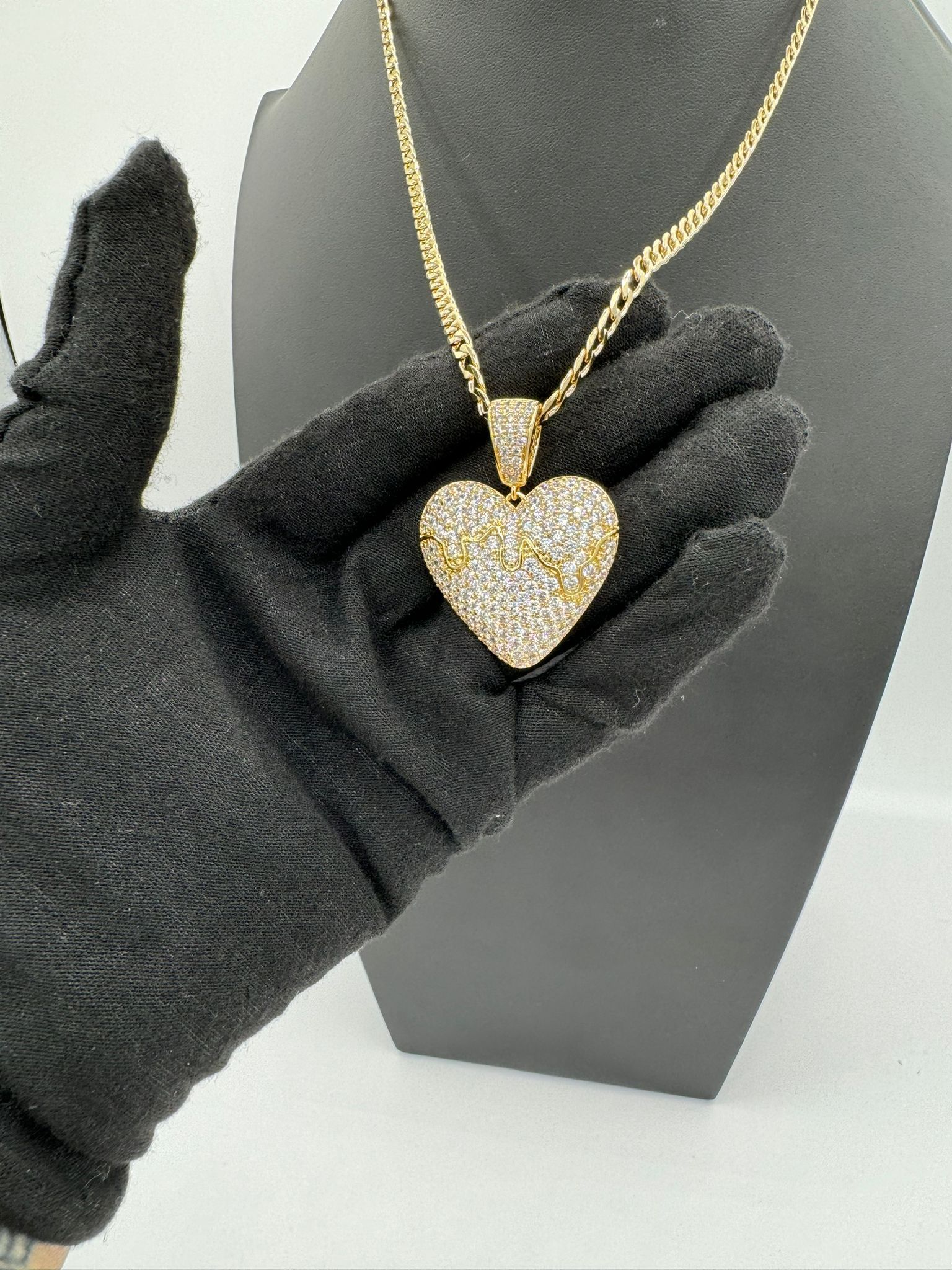 A person wearing a black glove is holding a necklace with a heart shaped pendant.