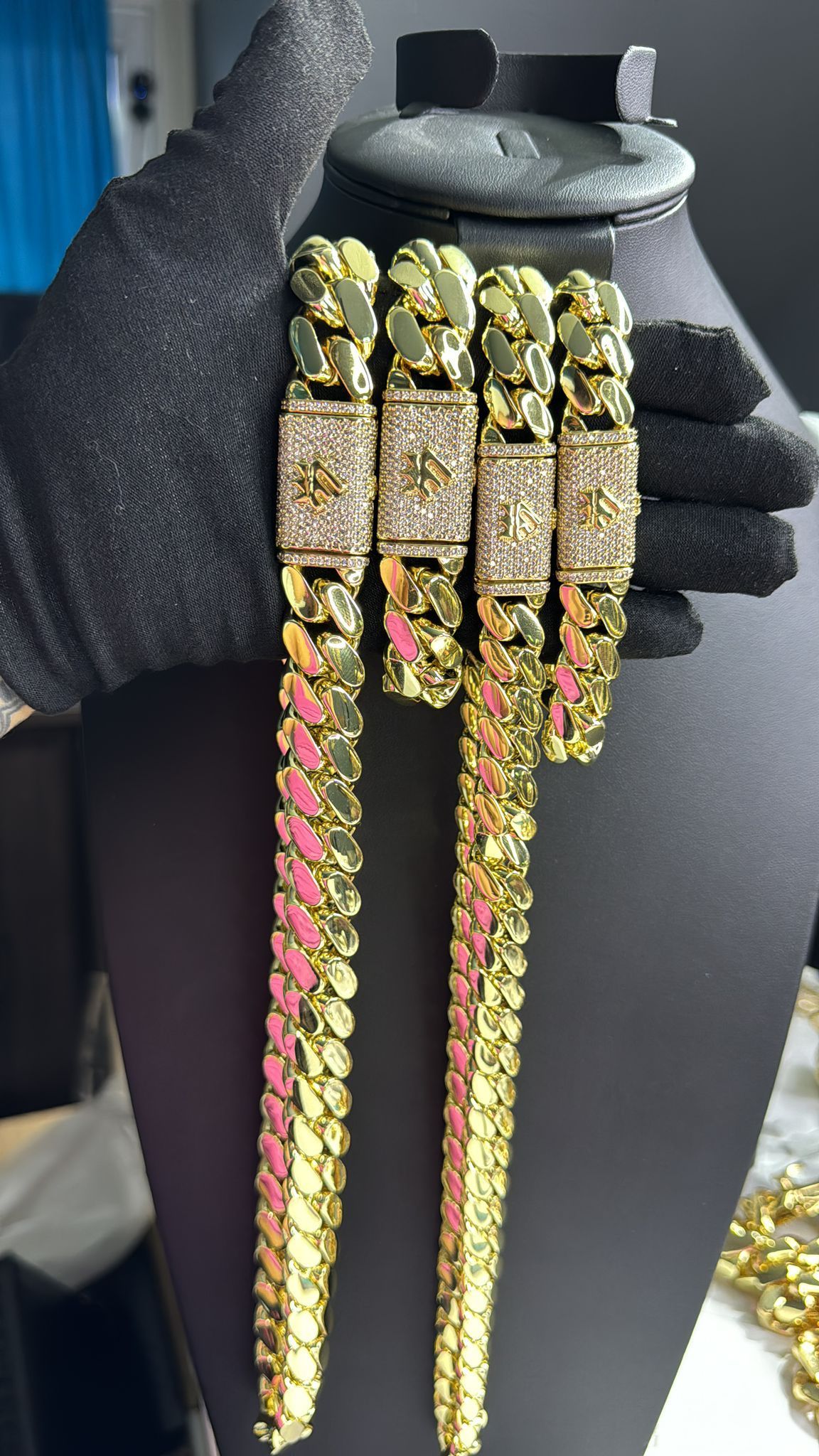 A person is holding three gold chains on a mannequin.