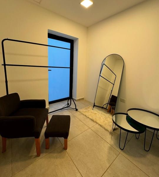 Un vestidor moderno con perchero negro, silla, espejo y mesas.