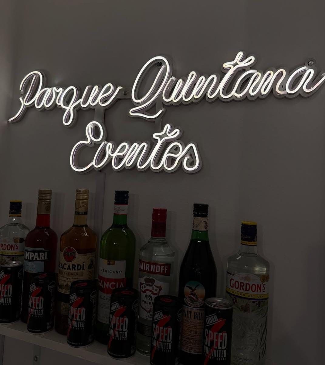 Letrero de neón “Parque Quintana Eventos” sobre botellas de licor y bebidas energéticas.