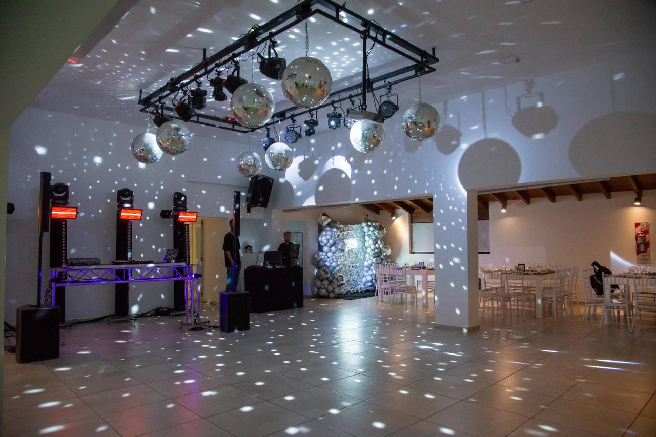 Un salón de baile con bolas de discoteca, iluminación de escenario y mesas preparadas para una fiesta.
