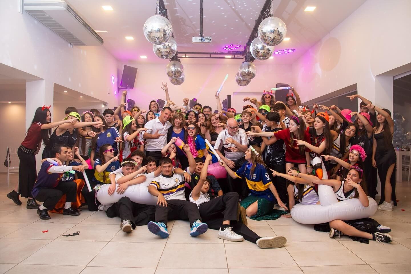 Un gran grupo de personas vestidas de fiesta posa en una habitación muy iluminada con bolas de discoteca.