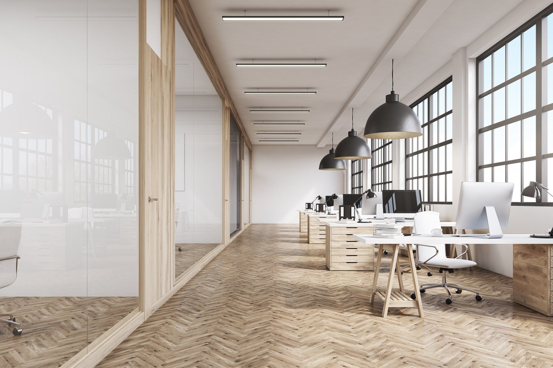 ffice interior with a row of dark wood tables standing under large windows.