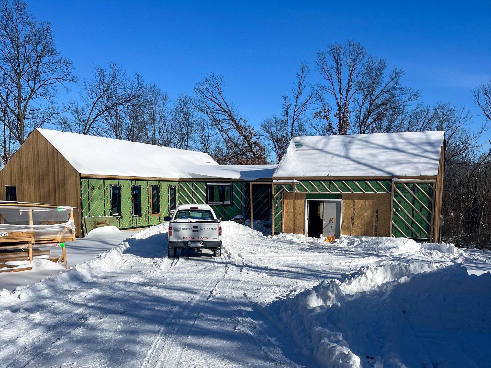 A white truck is parked in front of a house under construction covered in snow