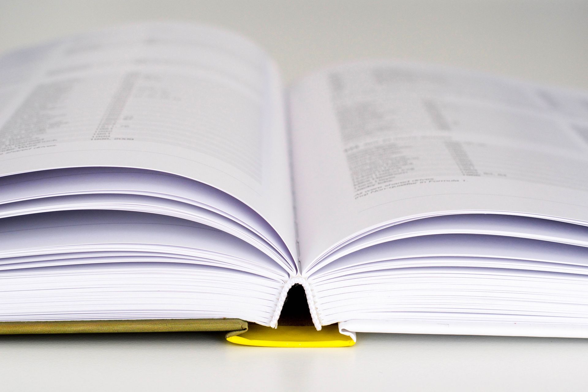 Open book with white pages and a yellow spine, resting on a surface.