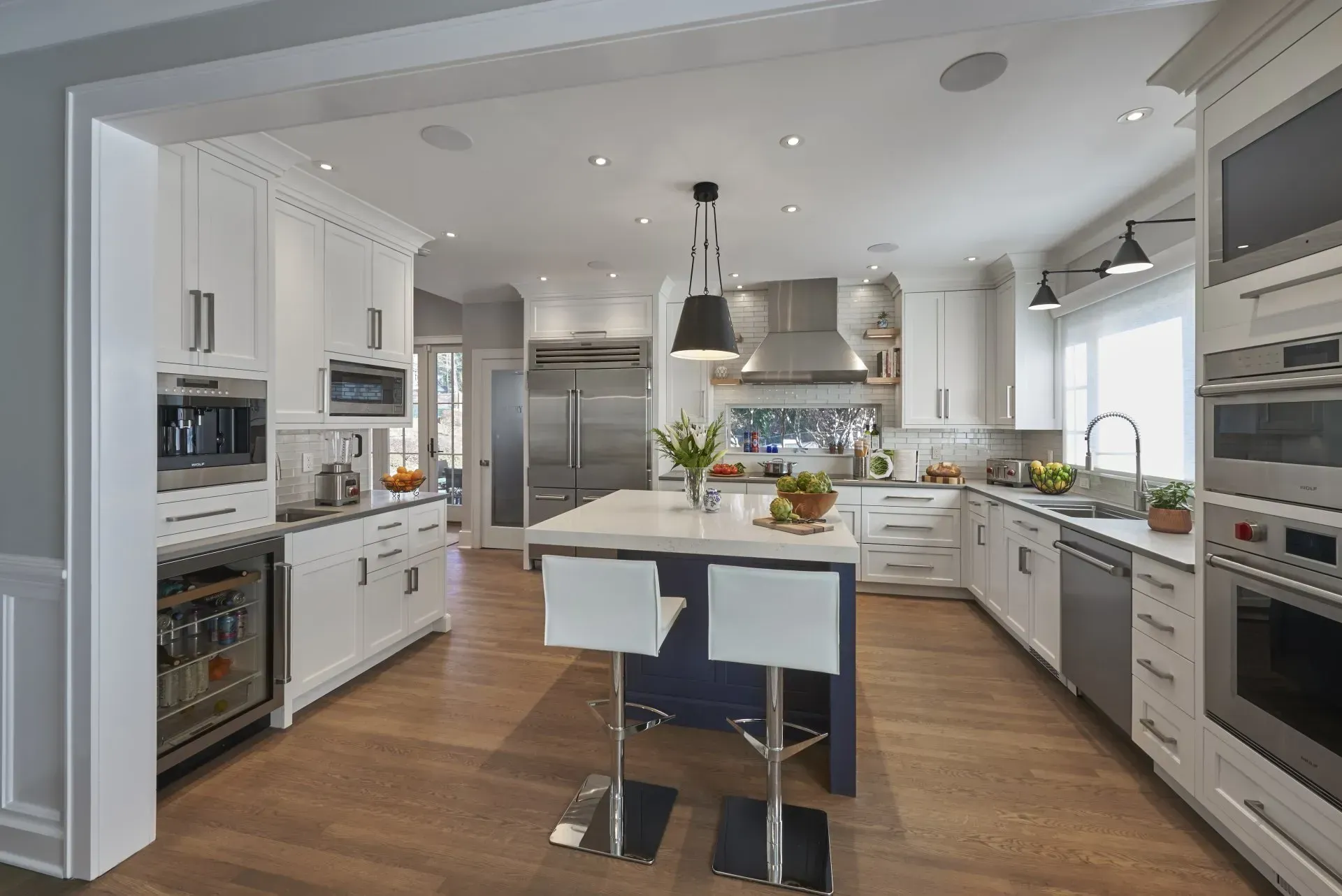Modern white kitchen with island, stainless steel appliances, and wood floors.