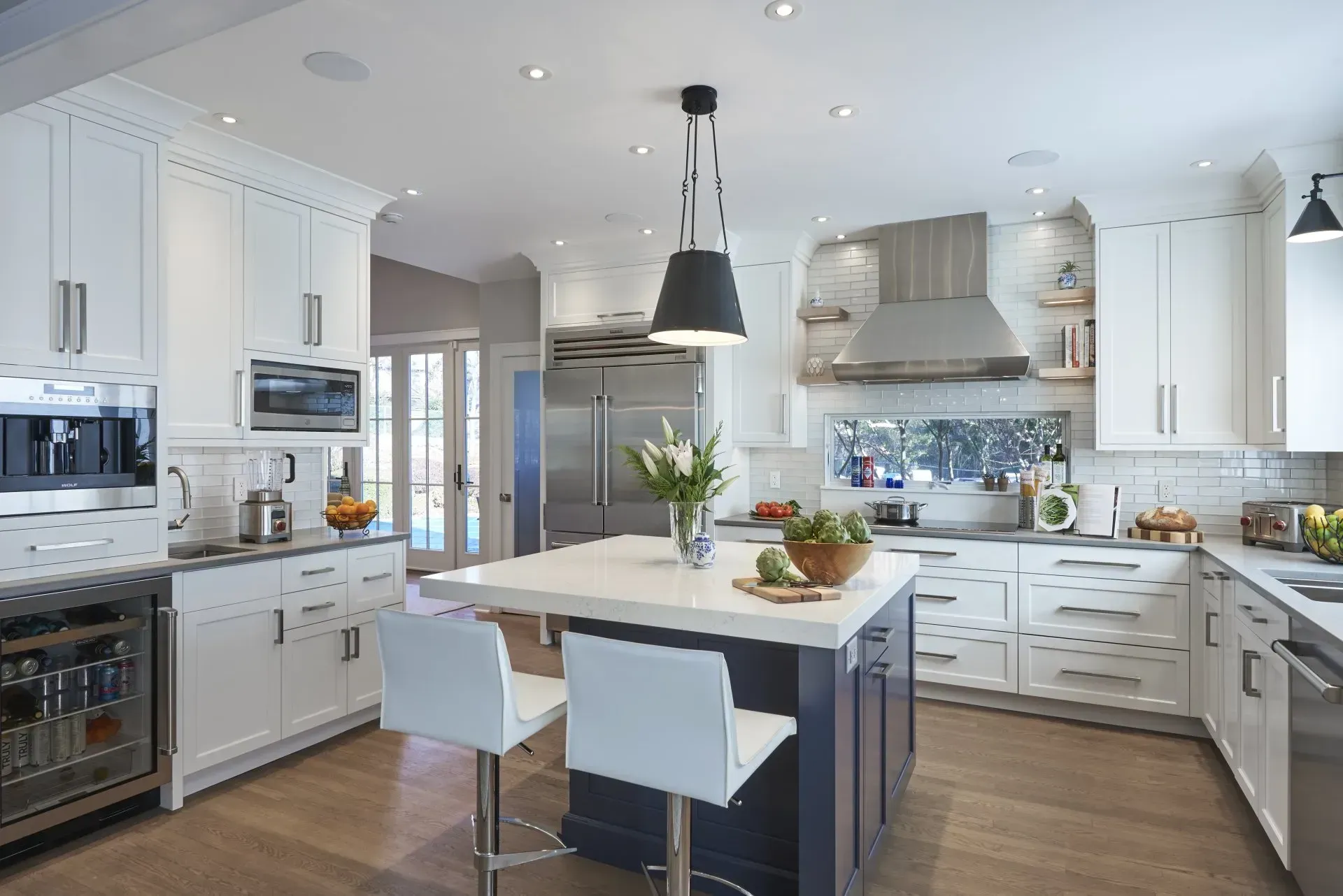 Modern white kitchen with a dark blue island and two white bar stools.