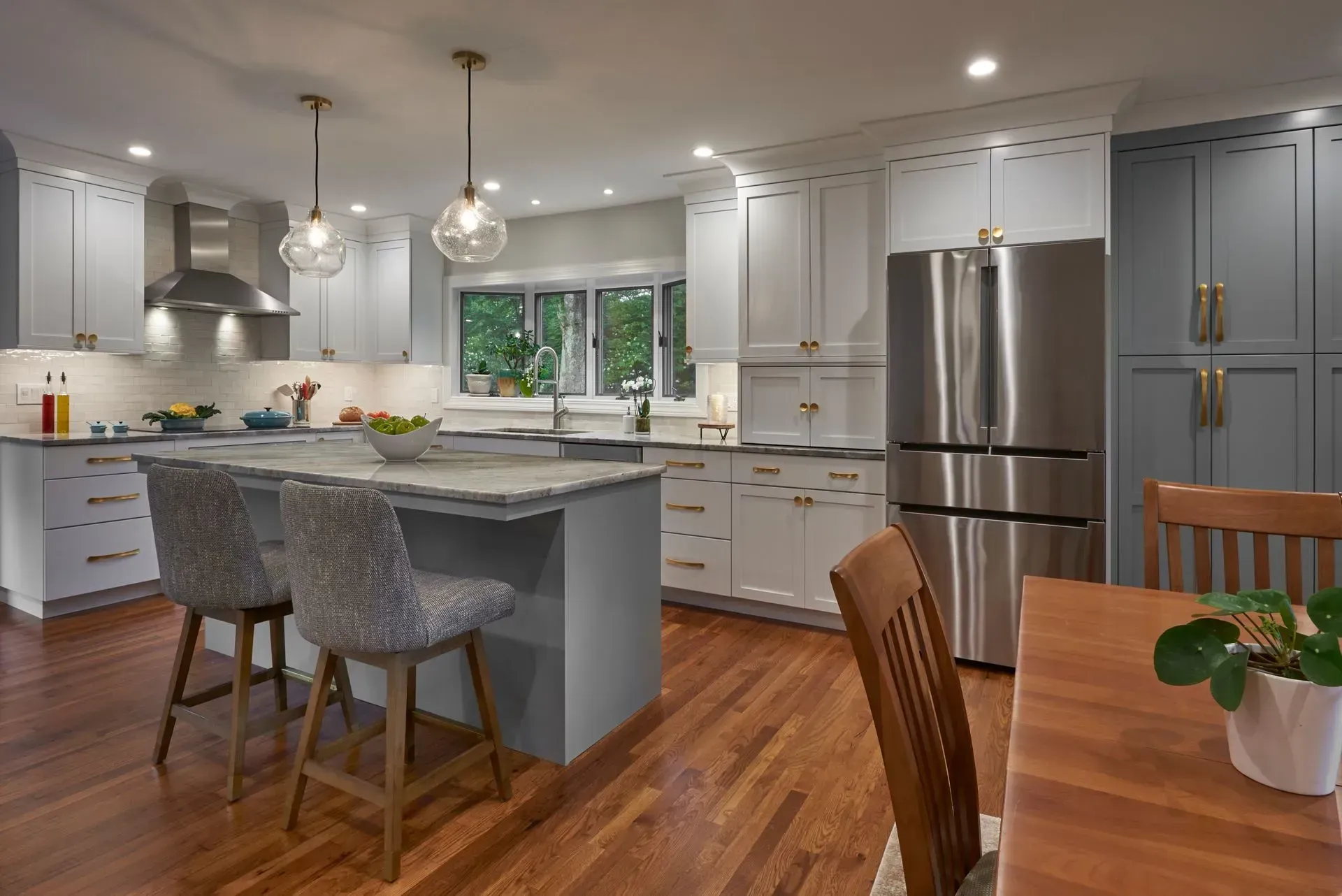 Modern kitchen with gray and white cabinets, stainless steel appliances, and wood flooring. Island with seating.