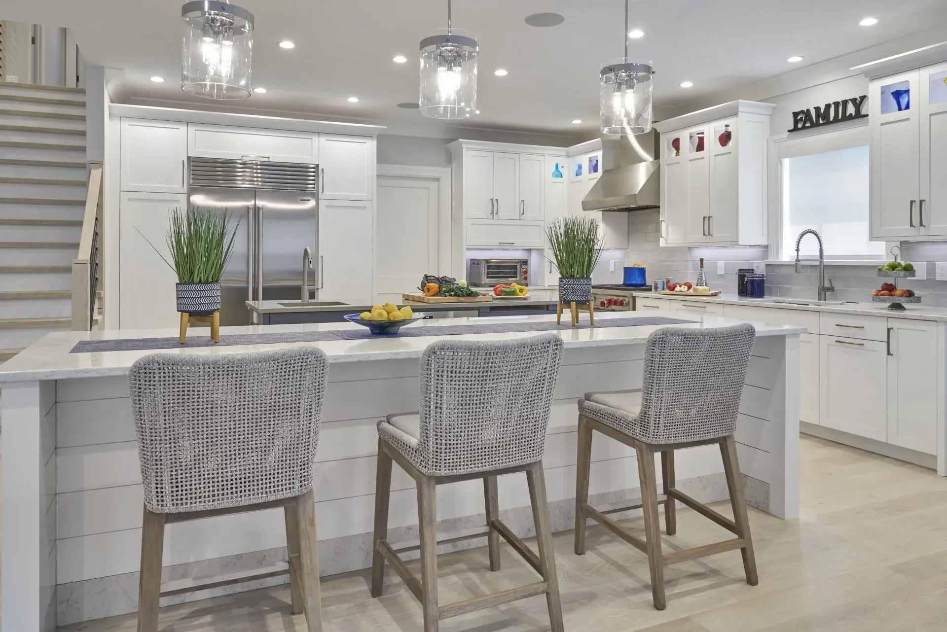 Modern white kitchen with island, seating, and stainless steel appliances.