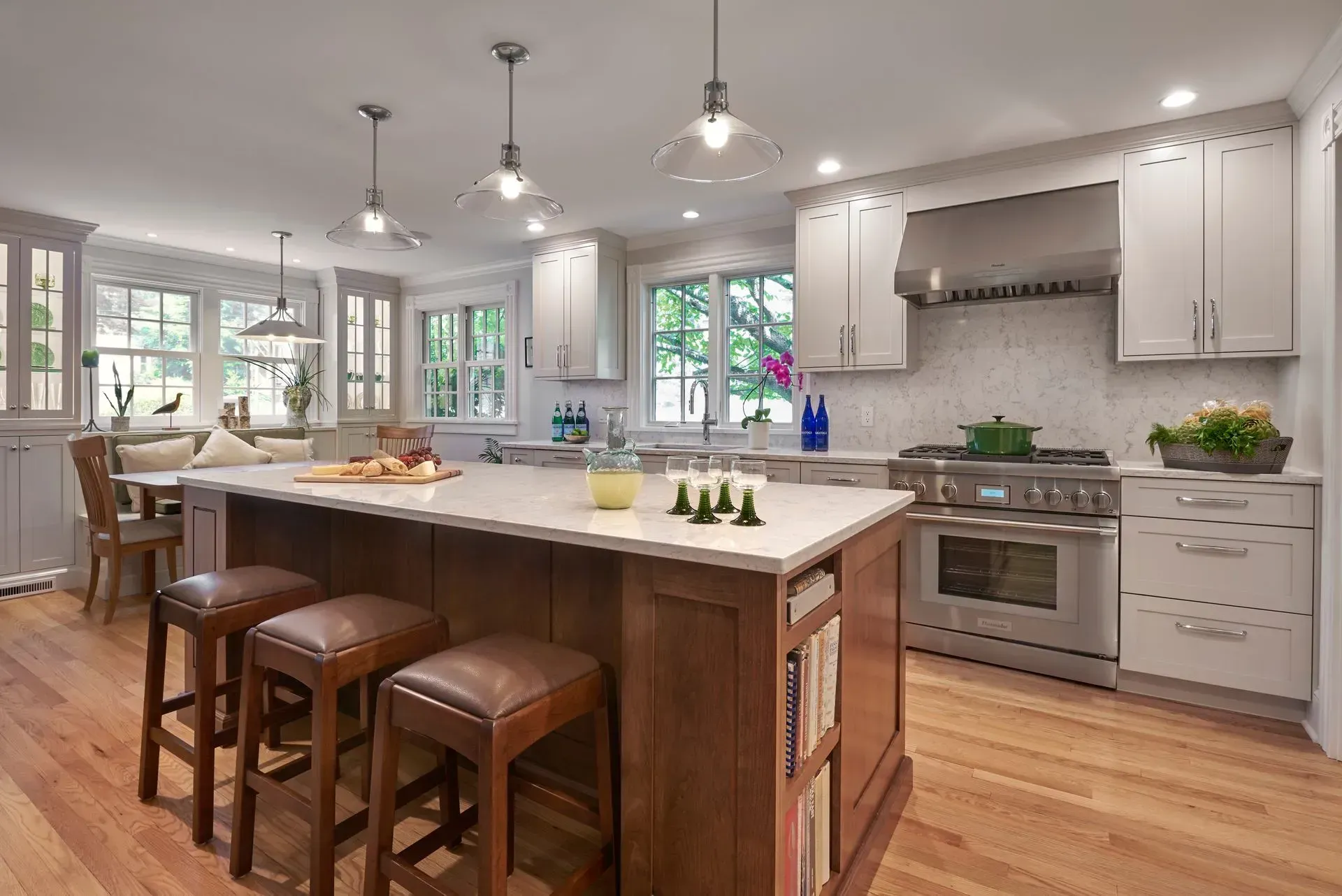A bright kitchen with an island and stools, stainless steel appliances, and wood floors.