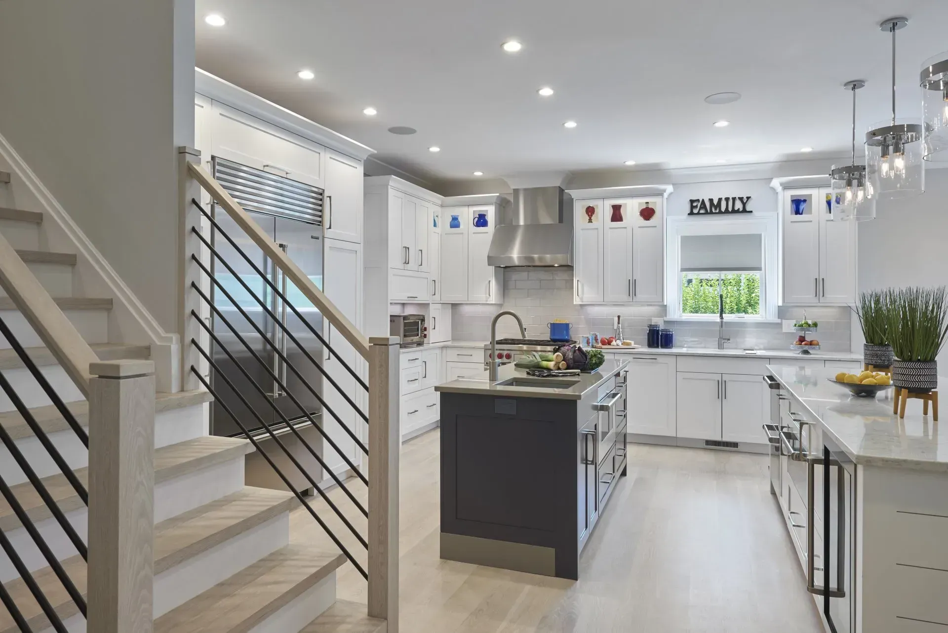 Modern white kitchen with island, stainless steel appliances, and staircase.
