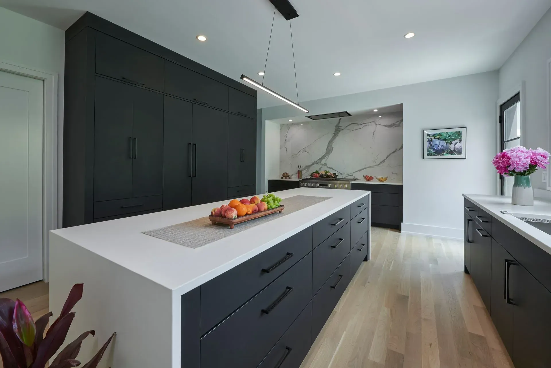 Modern kitchen with black cabinets, white countertops, and wood floors.