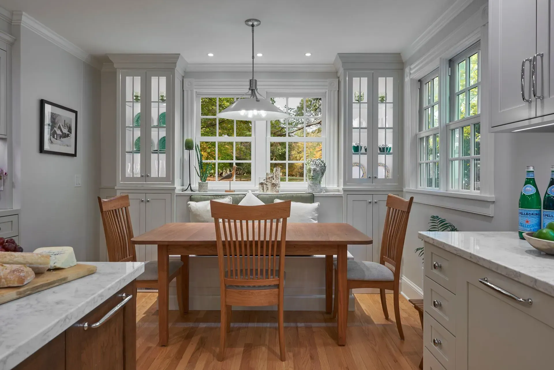 Kitchen with a wooden table, chairs, cabinets, and a window seat overlooking a yard.