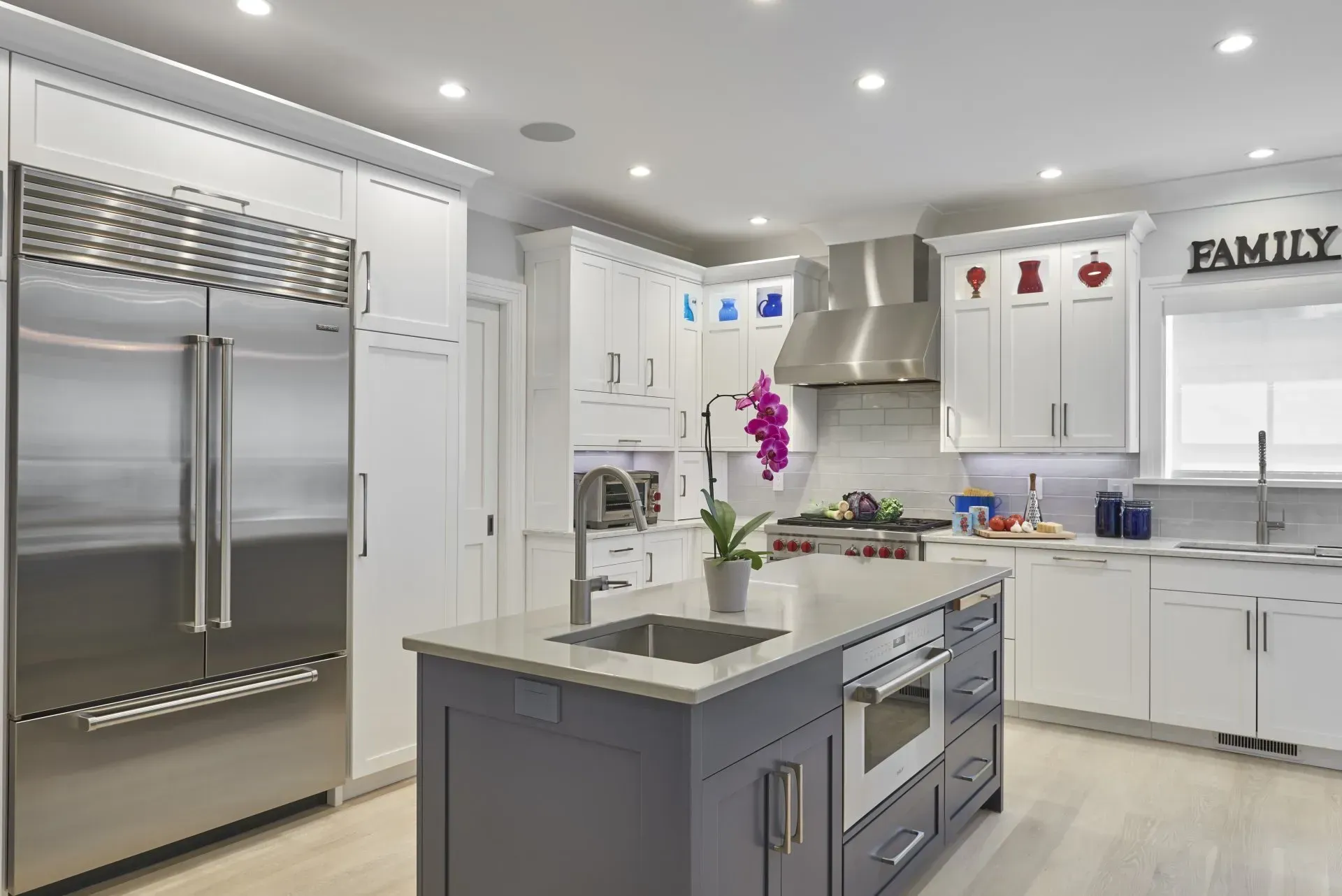 Modern kitchen with white cabinetry, gray island, stainless steel appliances, and overhead lighting.
