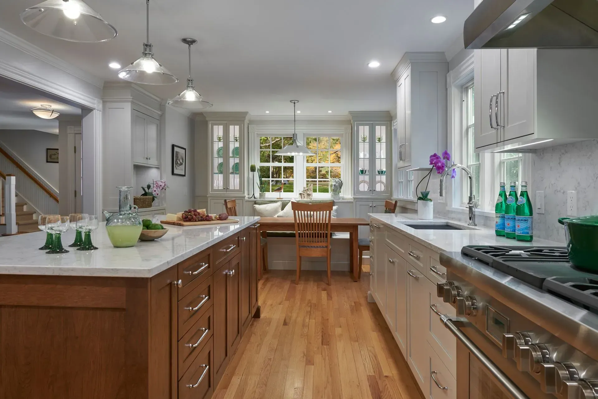 Spacious kitchen with a wooden island, white cabinets, and a gas range. Sunlight streams through a window.