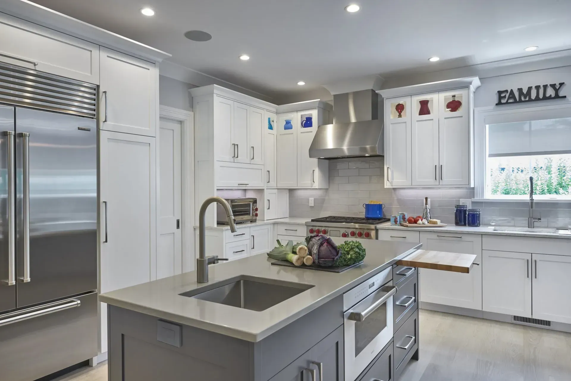 Modern kitchen with white cabinets, stainless steel appliances, grey island with sink.