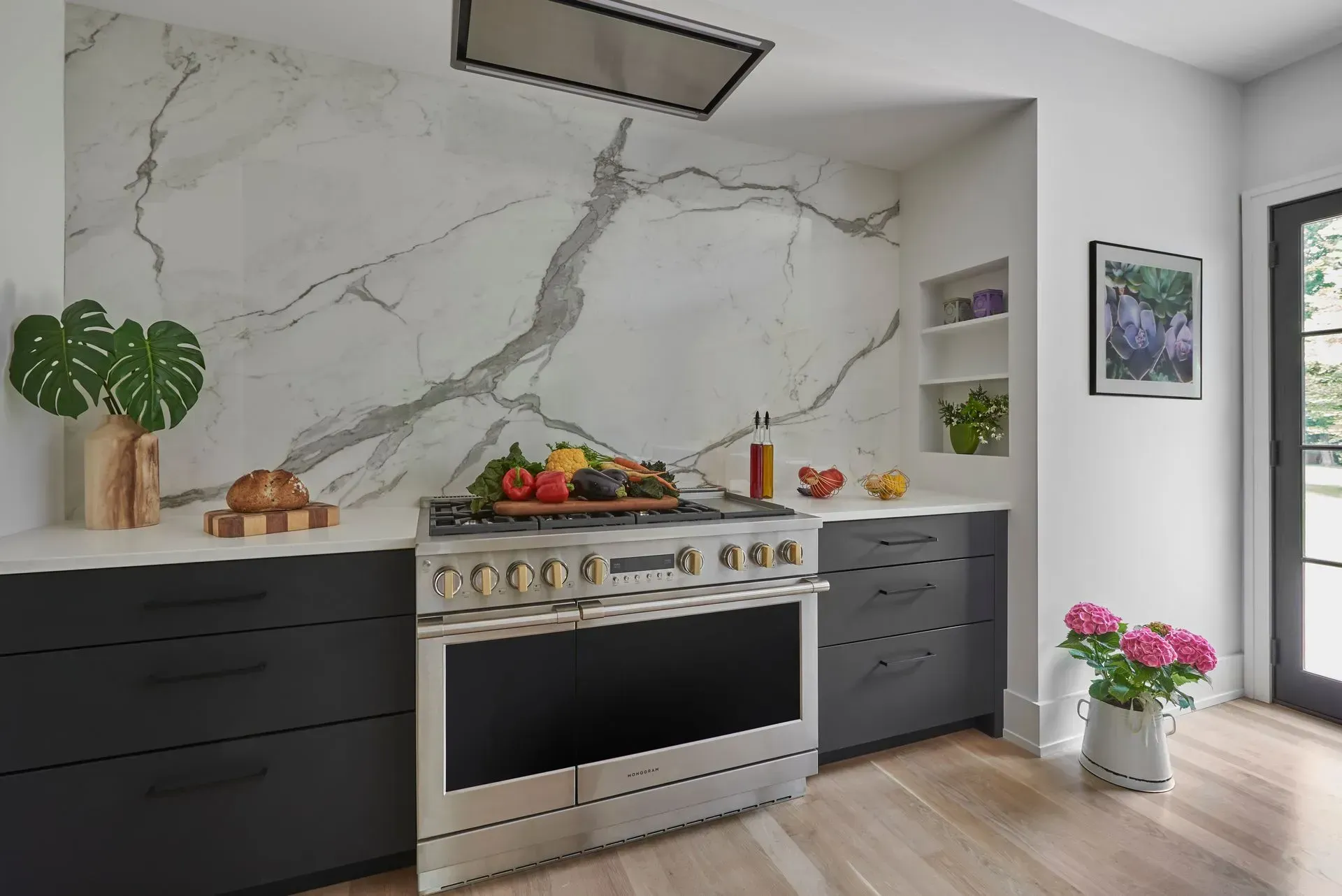 Modern kitchen with stainless steel oven, marble backsplash, and dark gray cabinets.