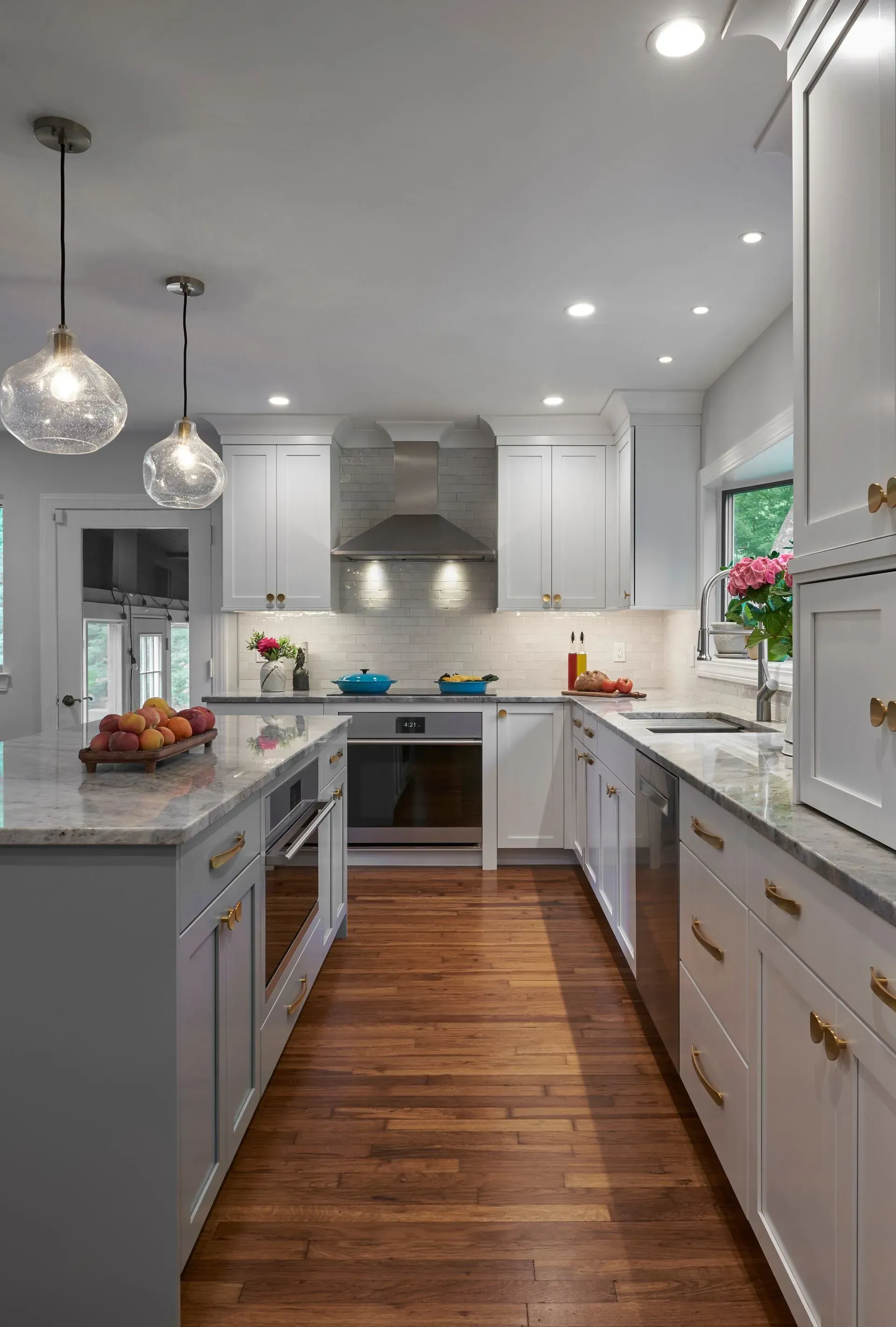 Bright kitchen with white cabinets, wood floor, island, and stainless steel appliances.