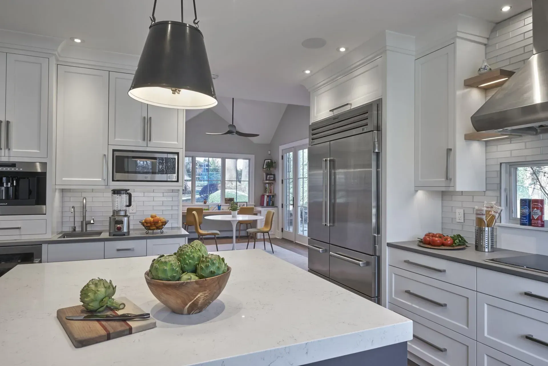 Modern white kitchen with stainless steel appliances, large island with artichokes, and view to dining area.