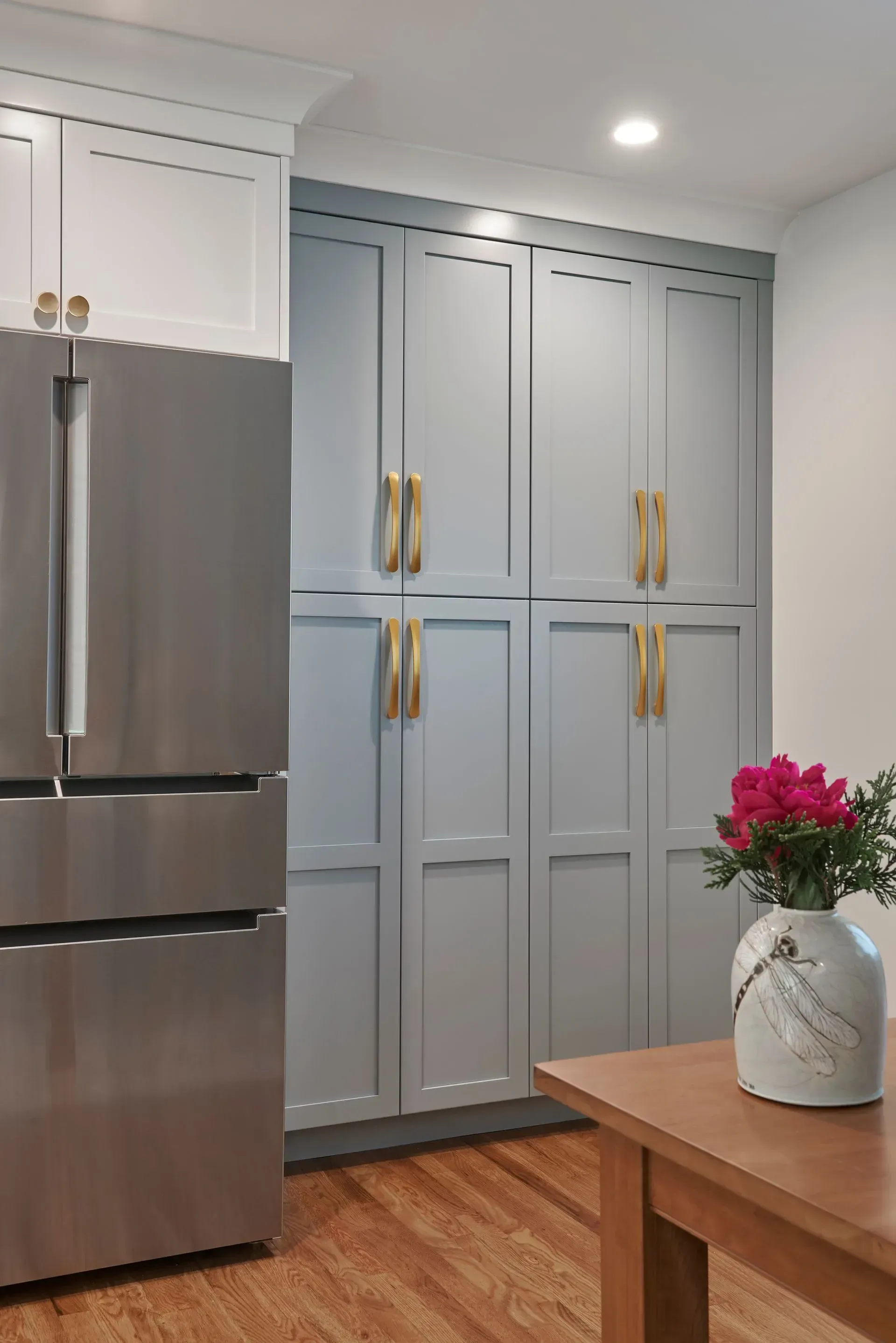 Stainless steel refrigerator next to gray pantry cabinets with gold handles in a kitchen.