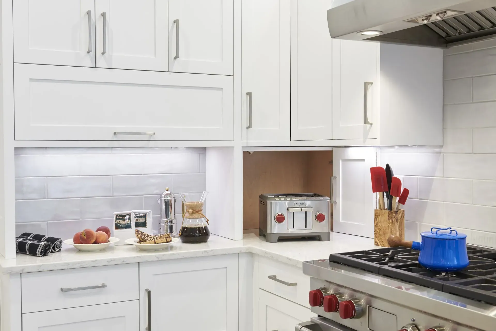 White kitchen with built-in toaster niche, white cabinets, stainless steel appliances, and tile backsplash.