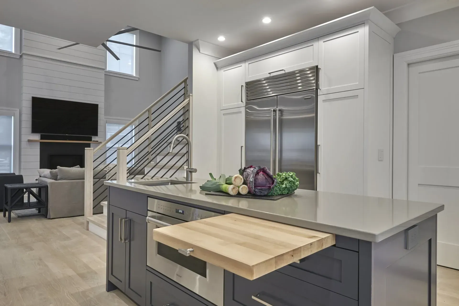 Modern kitchen with blue island and built-in microwave, stainless steel refrigerator, and wood cutting board.