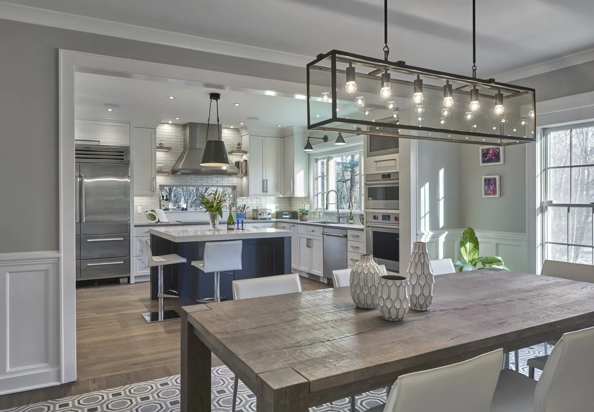 Open-concept kitchen and dining area with a navy island, stainless steel appliances, and a long wooden dining table.