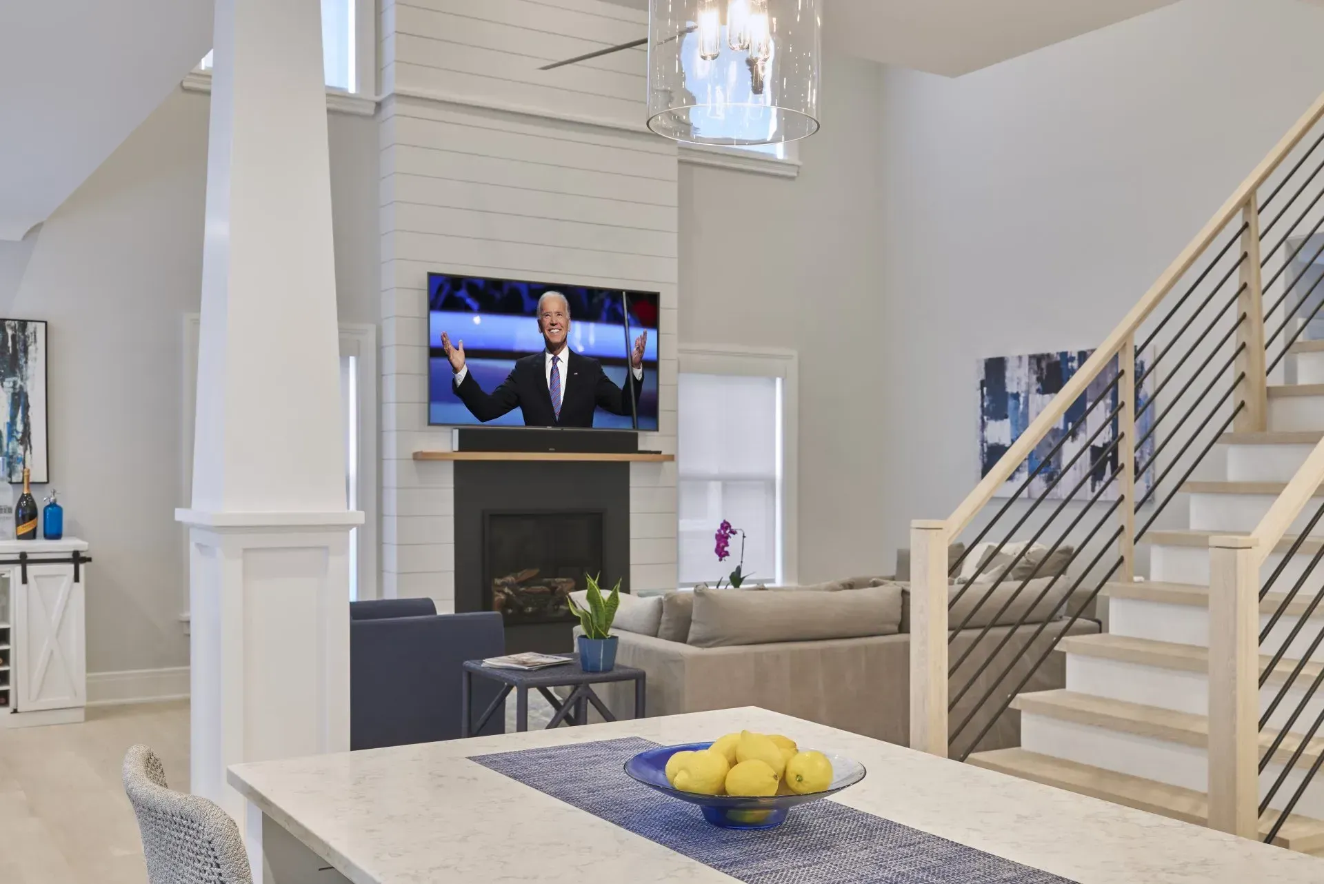 Bright, modern living room with TV over fireplace, staircase, and open kitchen with lemons.