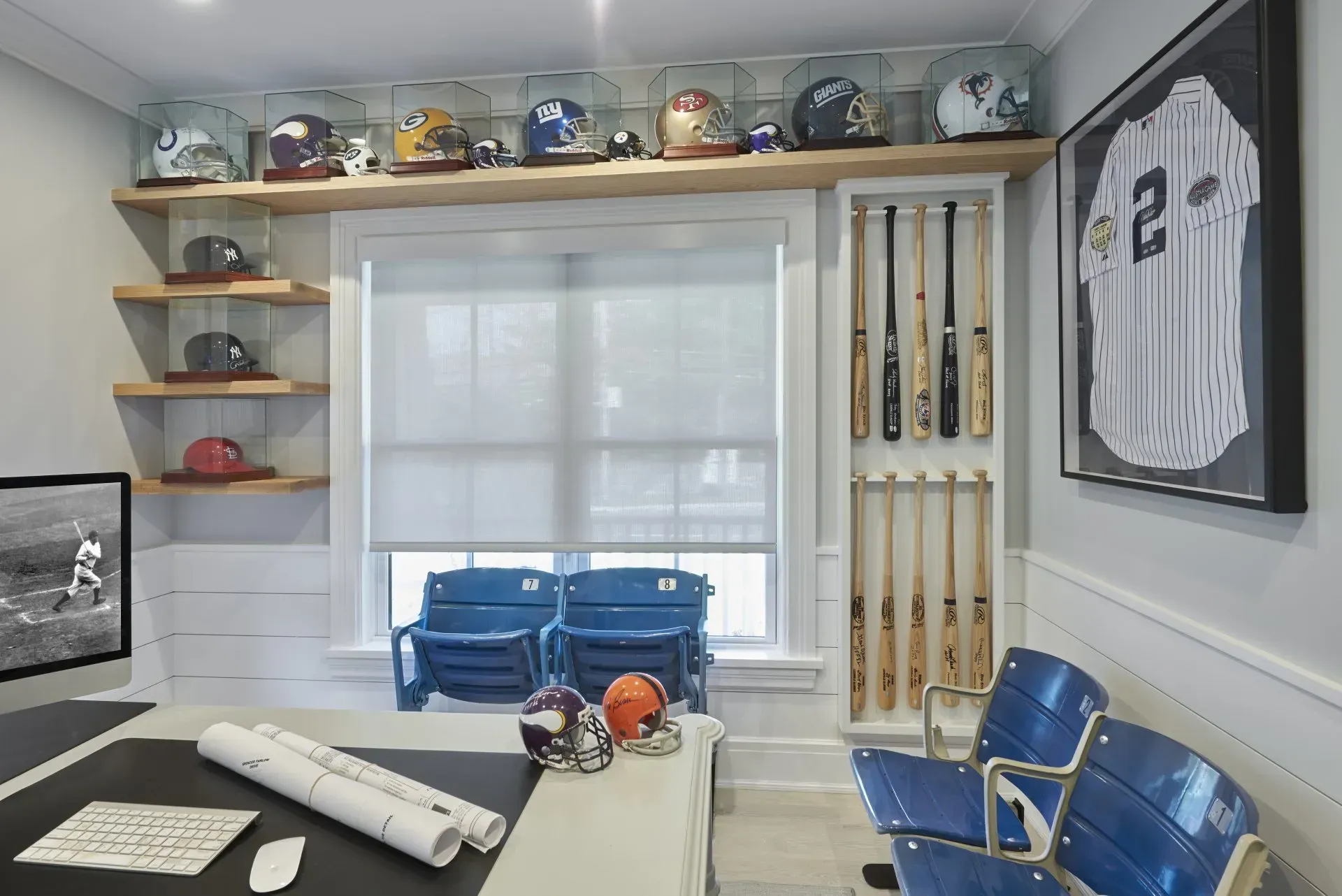 A sports-themed office with baseball bats, helmets, and framed jersey; blue seating, and a desk.