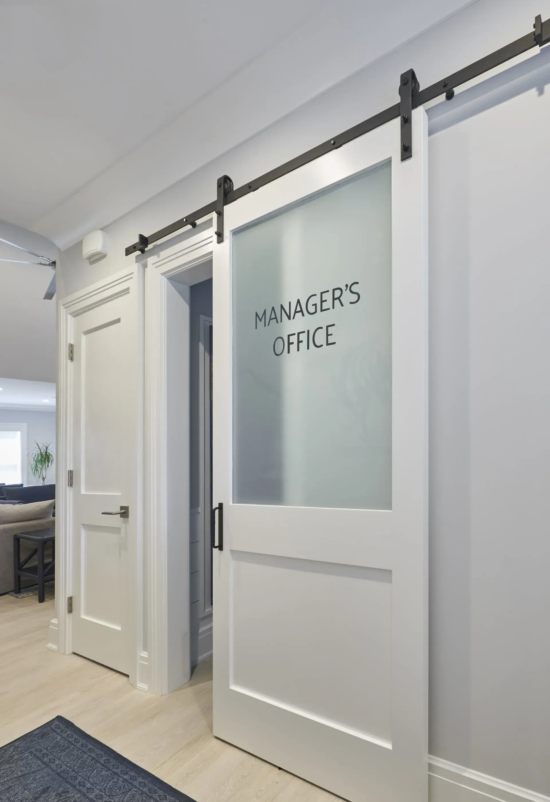 White barn door to manager's office with frosted glass, mounted on a black track in a hallway.