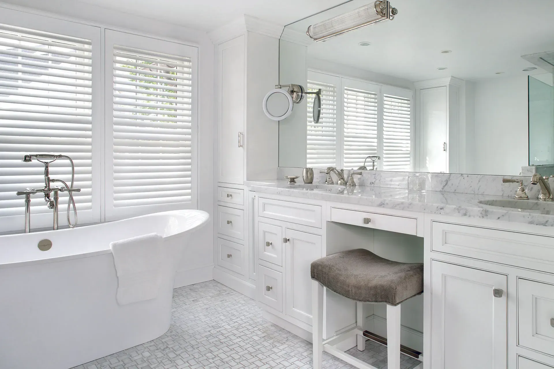 White bathroom with tub, vanity, shuttered windows, and marble countertops.