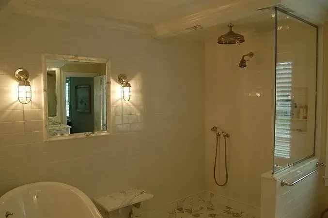 Bathroom with white tile, glass shower, sconce lighting, and a bathtub.