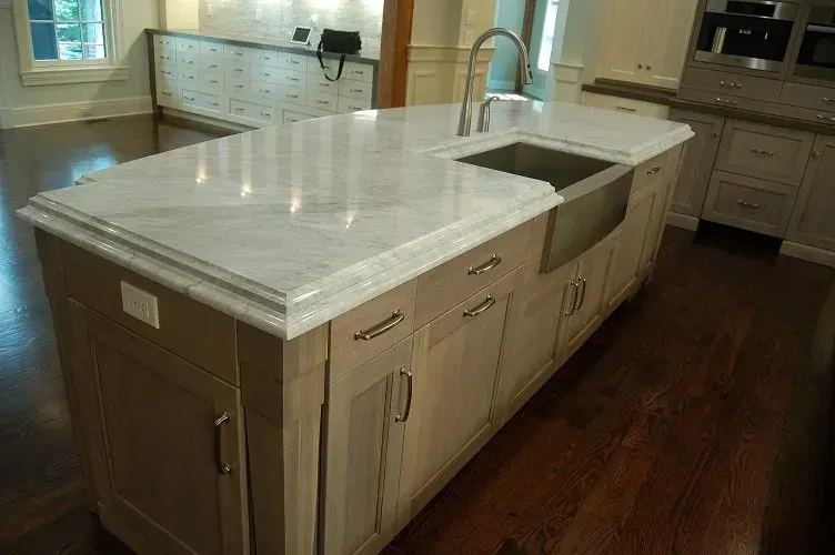 Kitchen island with marble countertop and stainless steel sink, light wood cabinets, and dark wood floor.