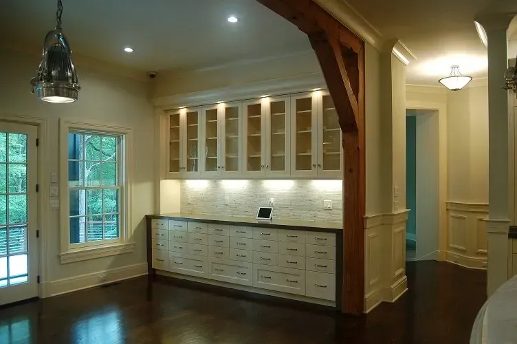 A well-lit room with built-in white cabinets, wooden post, and dark wooden floor.