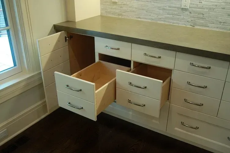 White kitchen cabinets with drawers open, countertop, and a window in the corner.