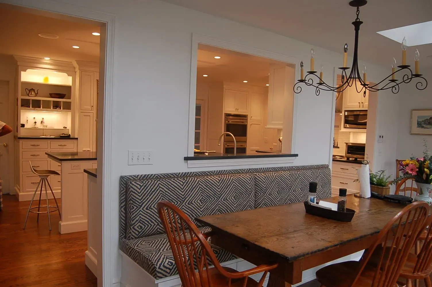 Kitchen with built-in bench seating, wood table, and pass-through window to another kitchen area.