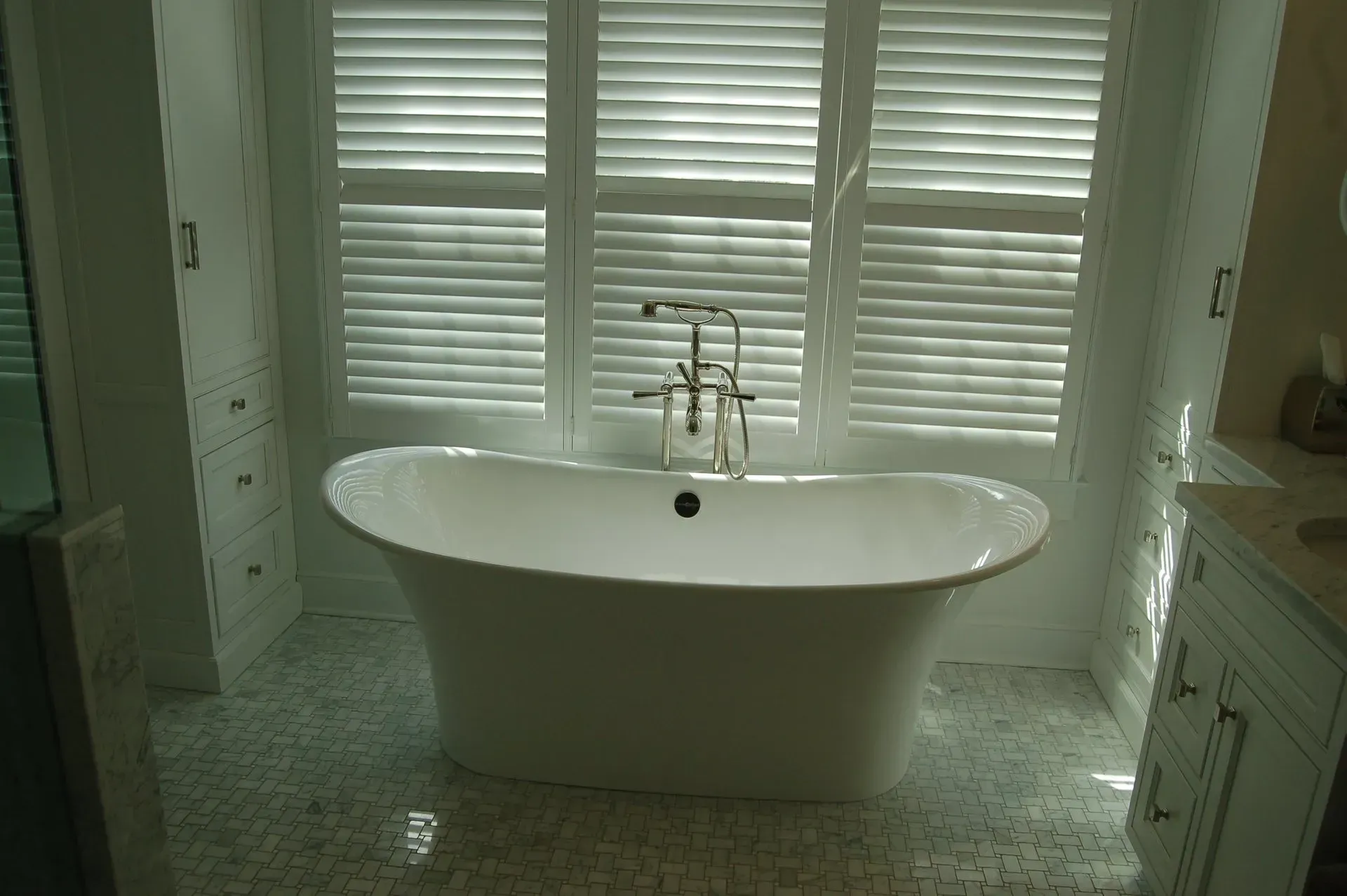 Bathroom with a white freestanding bathtub, mosaic floor, and shuttered windows.