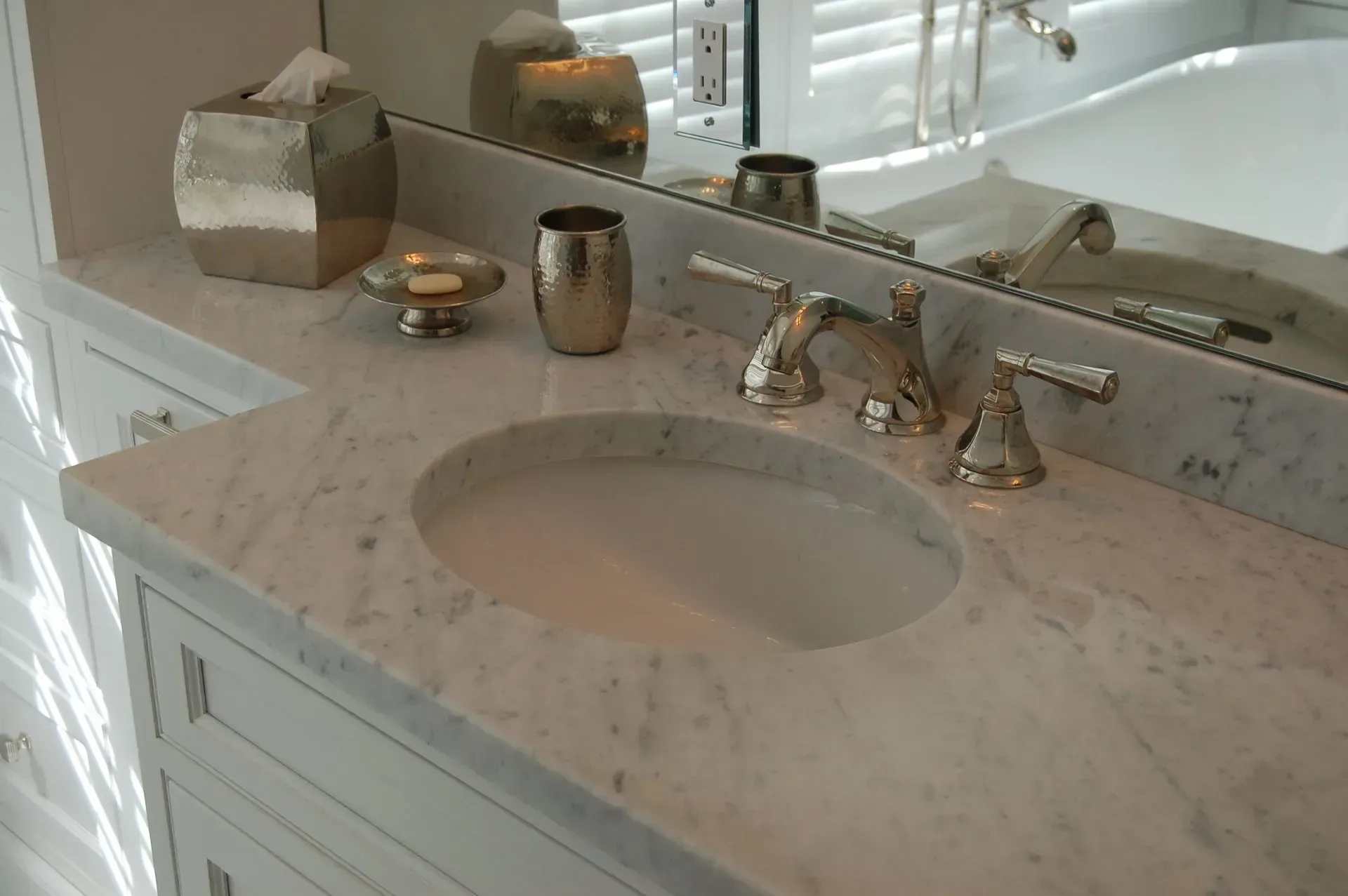 White marble bathroom vanity with oval sink, gold fixtures, and accessories.